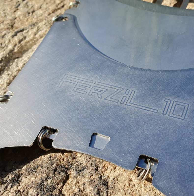 Bushbox Ferzil 10 avec paravent, posé sur une pierre, un pare-vent autour. Une petite tasse à café posée dessus.